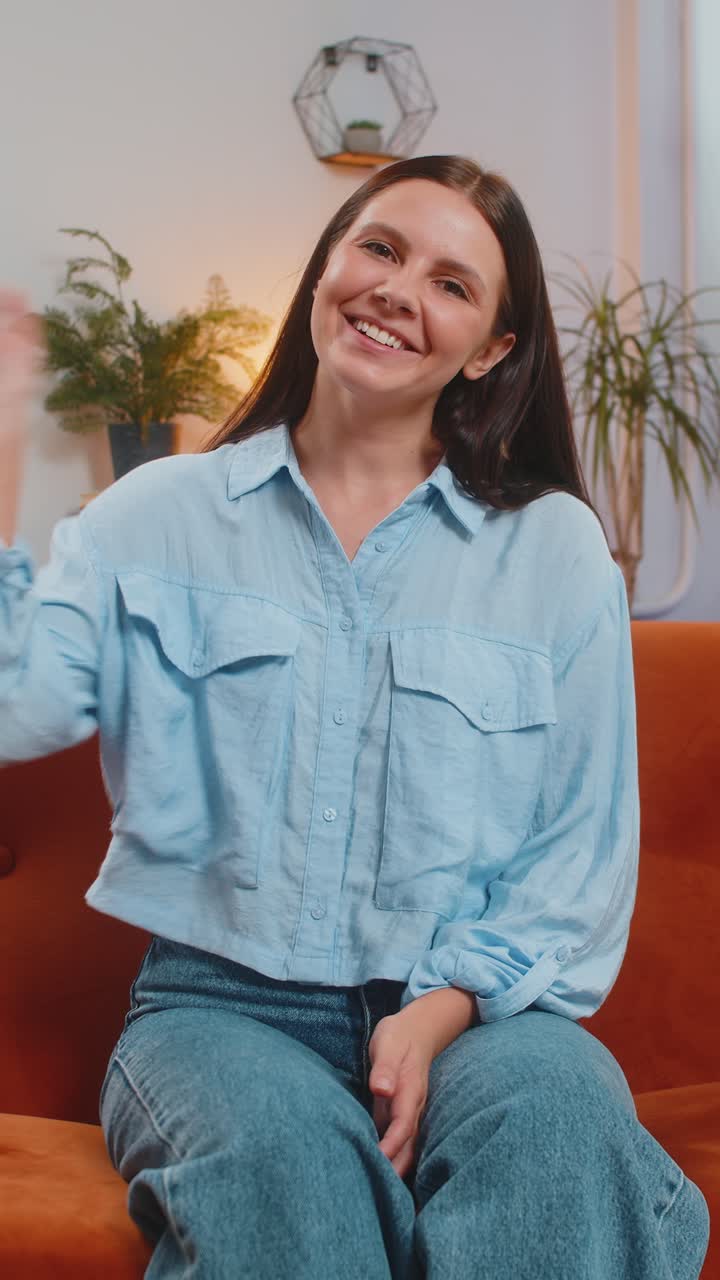 Woman smiling friendly at camera and waving hands gesturing hello hi greeting talking at home