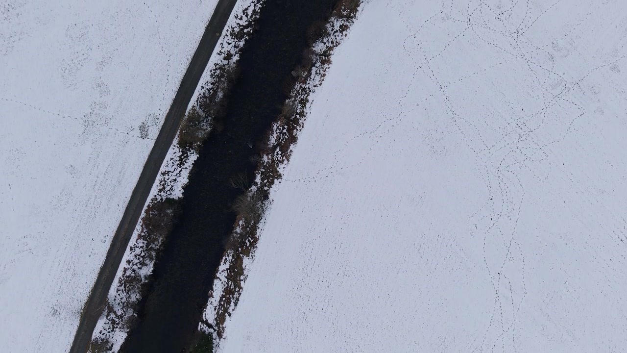 A snow-covered field with a winding stream and visible tracks. Perfect for winter-themed projects or geographic documentaries.