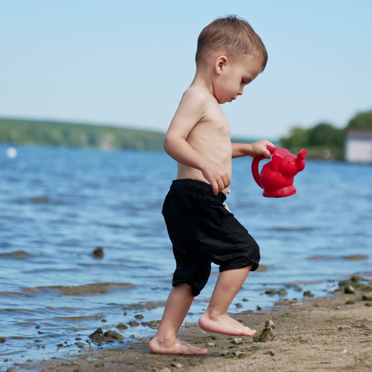 Beautiful Caucasian toddler playing in the beach. Kid carries a watering can filled with water from river