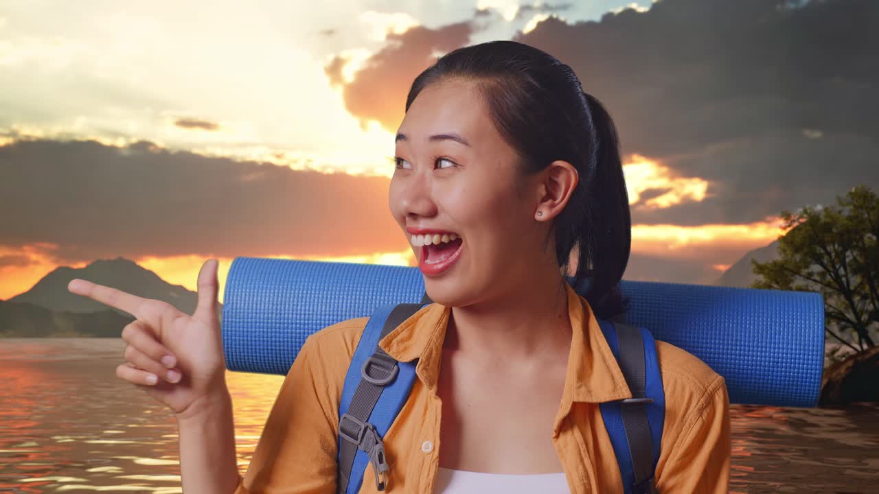 Close Up Of Asian Female Hiker With Mountaineering Backpack Smiling And Pointing To Side While Standing At A Lake During Sunset Time