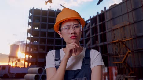 close up of asian woman worker wearing goggles and safety helmet thinking about something and looking around while standing at construction site