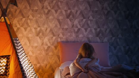 una niña nerviosa se rasca el cuadrilátero en la cama cerca de un wigwam de juego