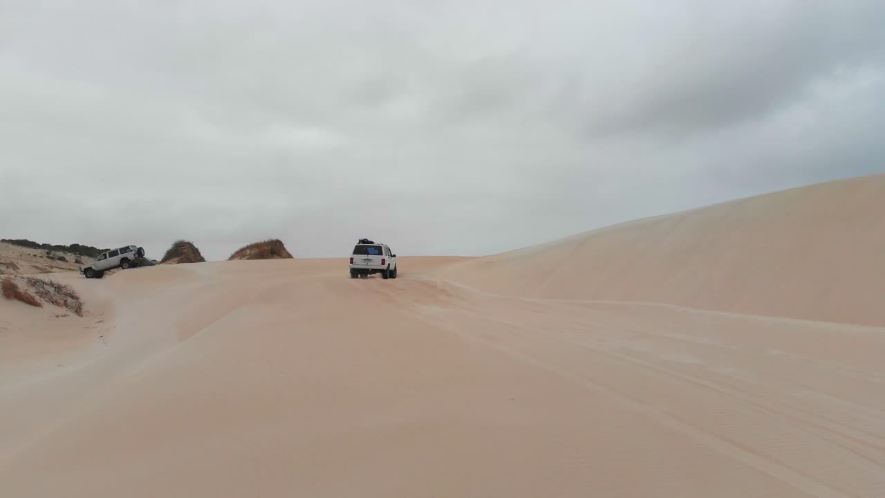 구름이 많은 날 에 오스트레일리아 의 제럴드턴 에 있는 모래 언덕 을 가로질러 이동 하는 자동차 들 의 그룹