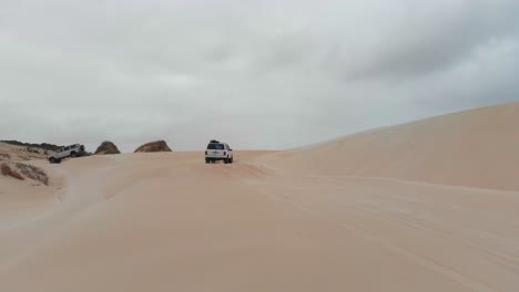 Group-of-cars-cruising-on-dunes-at-Geraldton-Australia-on-cloudy-day,-aerial