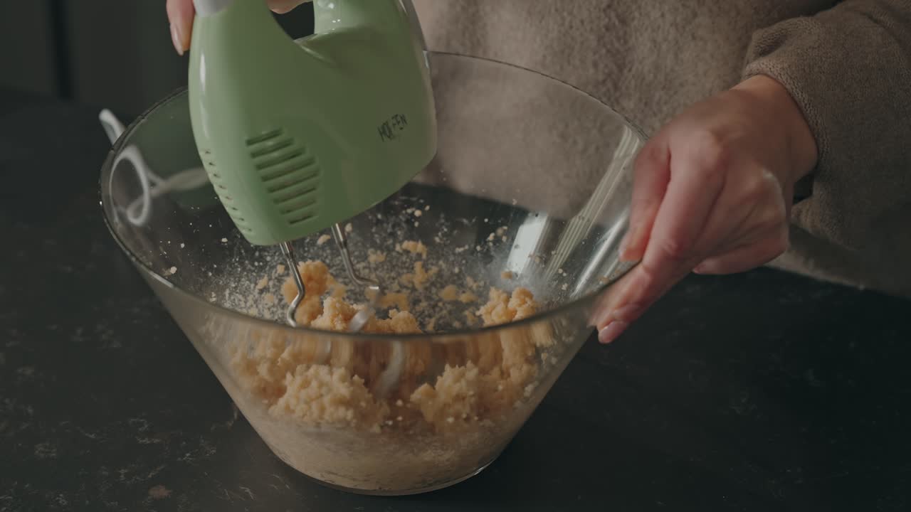 Primo piano di uno sbattitore elettrico a mano che mescola ingredienti da forno in una ciotola trasparente, all'interno.