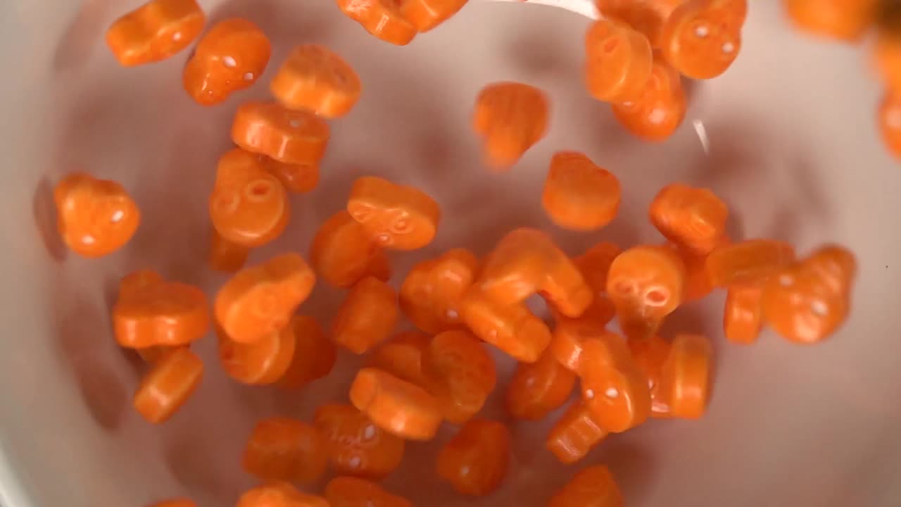 cerca de caramelos con forma de calaveras naranjas cayendo sobre un plato