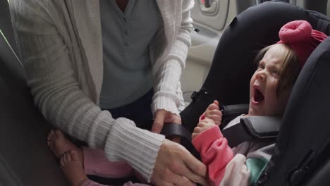 mid section of caucasian mother keeping her baby in safety seat in the car