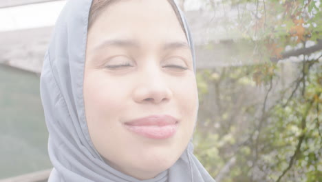 animation of leaves over biracial woman in hijab smiling