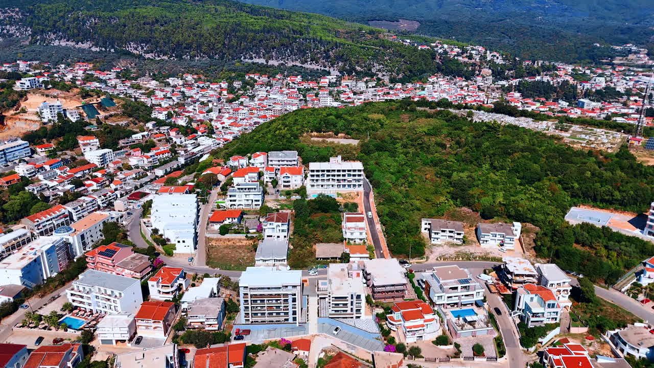 Approaching the verdant mountain almost covered with residential houses. Rocky landscape of Montenegro on sunny day. Aerial view