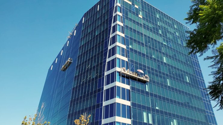 Operai puliscono le finestre di un edificio per uffici da un'impalcatura sospesa.