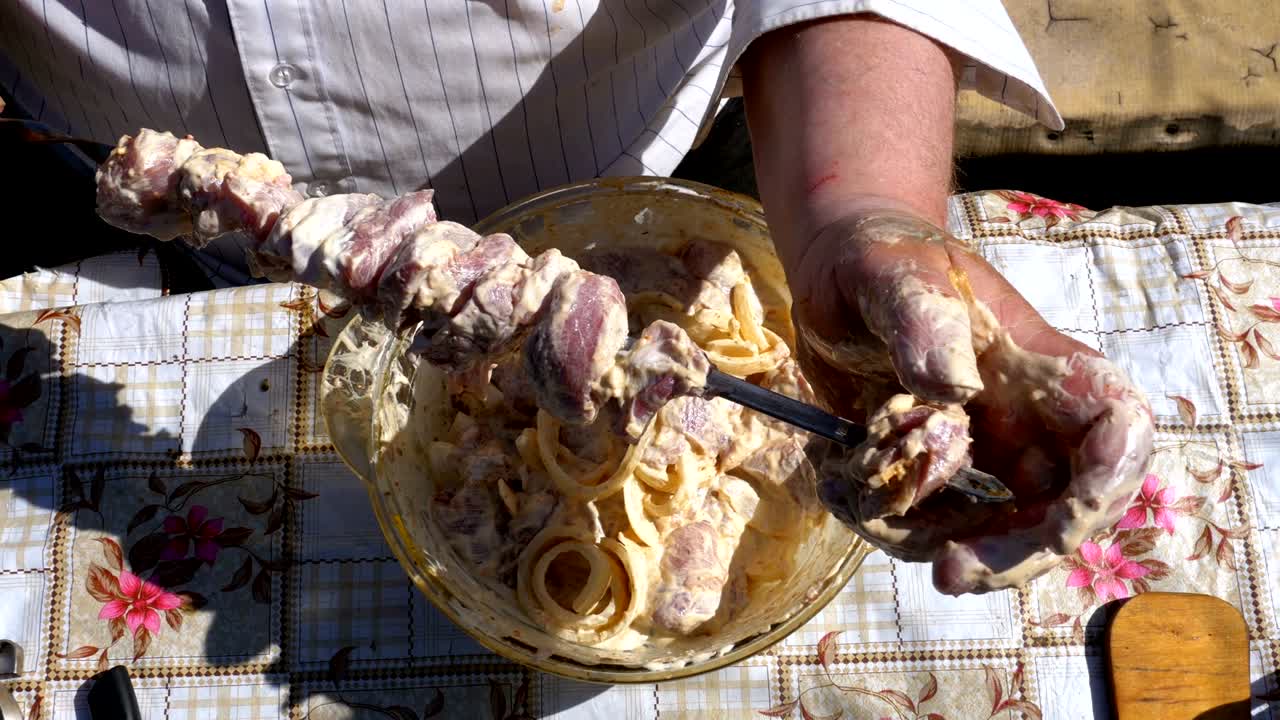el hombre gordo pone la carne cruda marinada en un pinchazo para un shish kebab en la naturaleza