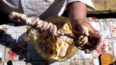 fat man puts the marinated raw meat on a skewer for a shish kebab on nature