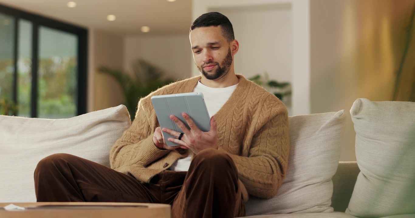 Young Man Using a Tablet While Sitting on a Sofa at Home