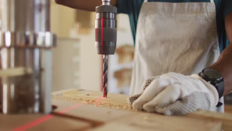 sección media de un carpintero afroamericano perforando madera con un taladro láser en un taller de carpintería