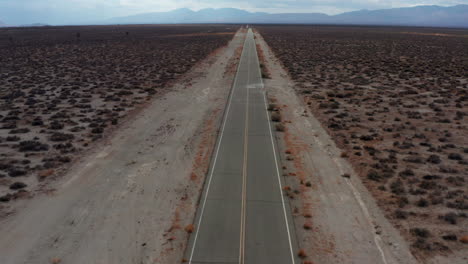 un camino vacío y solitario a través del calor del desierto de mojave - vista aérea inclinada hacia arriba con montañas más allá de la cuenca plana