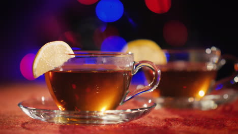 two cups with aen stand on the table against the background of the blurry lights of a christmas tree