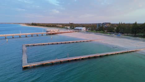 drone rising over busselton jetty sea baths to show aerial view of town in western australia at sunset