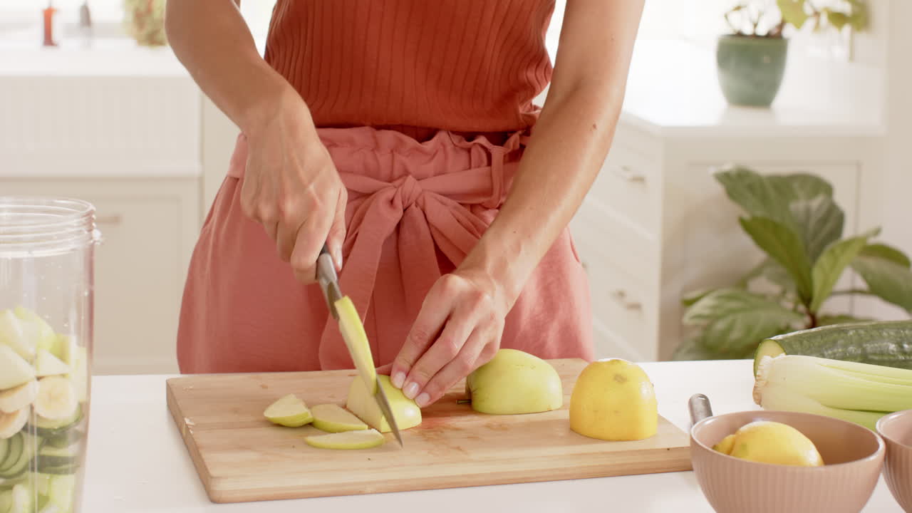 Woman slicing green apples on wooden cutting board in bright kitchen