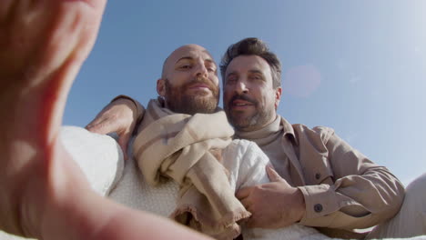 pov of a happy gay couple kissing and taking selfie on phone on the beach