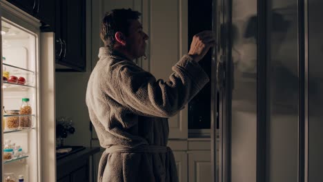 man in bathrobe eating late night snacks in kitchen