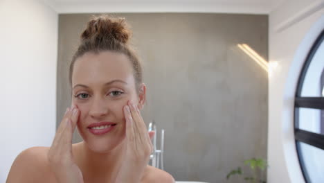 applying skincare, young woman smiling and touching face in bathroom, copy space