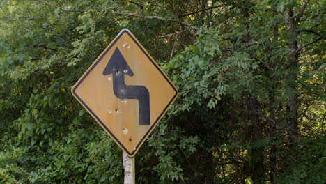 A medium close up shot of a road warning sign that has been vandalized by multiple gun shots along a rural road in the Ouachita national forest Arkansas