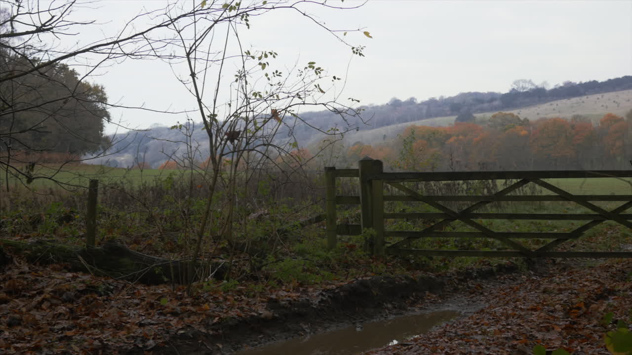 A PANNING SHOT of a closed wooden gate on a pathway in the English countryside, on a grey day