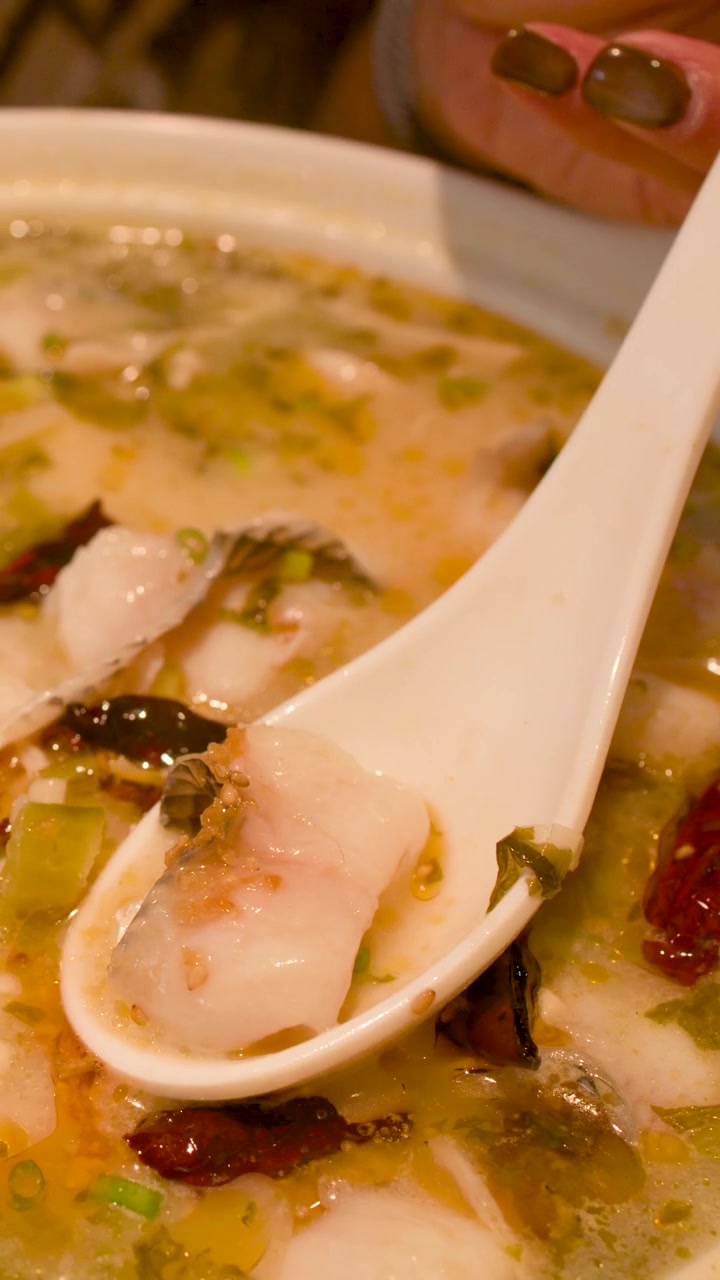 Nærbillede af en person, der øser krydret fiskenudelsuppe med en keramisk ske og træspisepinde.