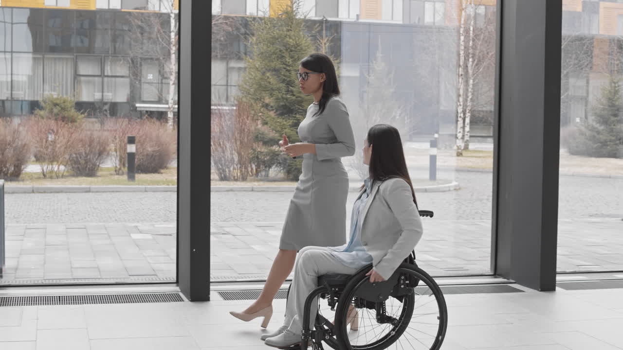 Businesswoman with Disability and Female Colleague Going along Office