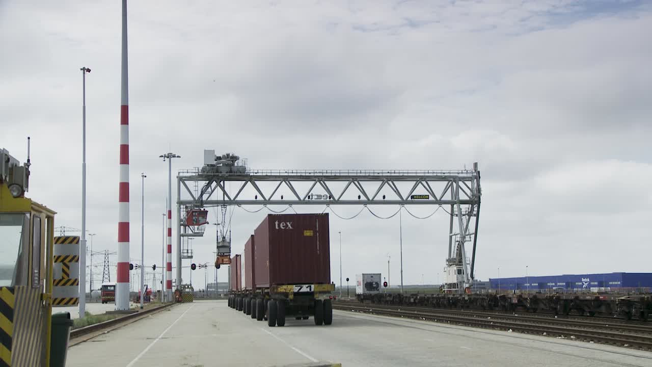 Container truck driving under a crane at a busy shipping port on a cloudy day