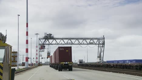 container truck driving under a crane at a busy shipping port on a cloudy day