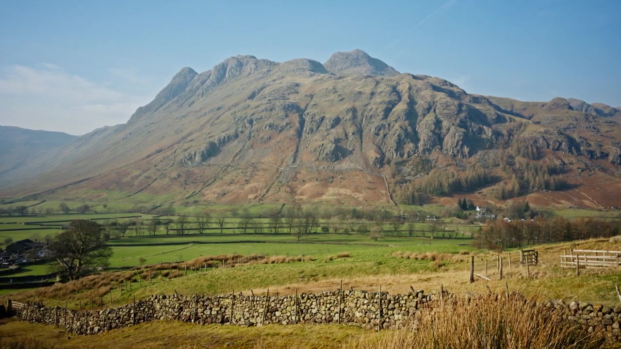 Dramatisk bjerg tårner sig op over grønne landskabsmarker og traditionelle stenmure, hvilket skaber et naturskønt landskab på landet i Great Langdale, England.