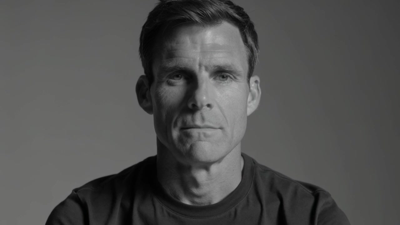 Camera rolling, man opening eyes, blinking, holding steady gaze in studio, gray backdrop dark tee