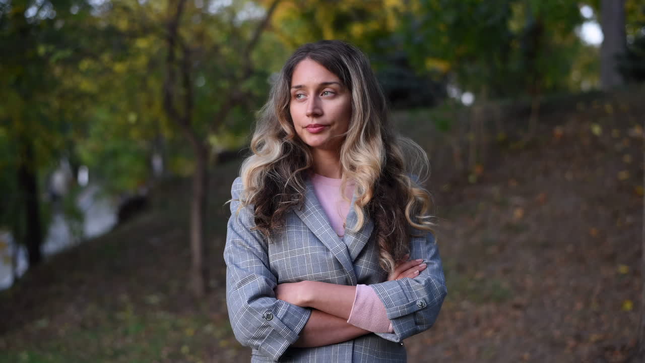Close up of a blonde woman in a grey blazer smiling at the camera in the park