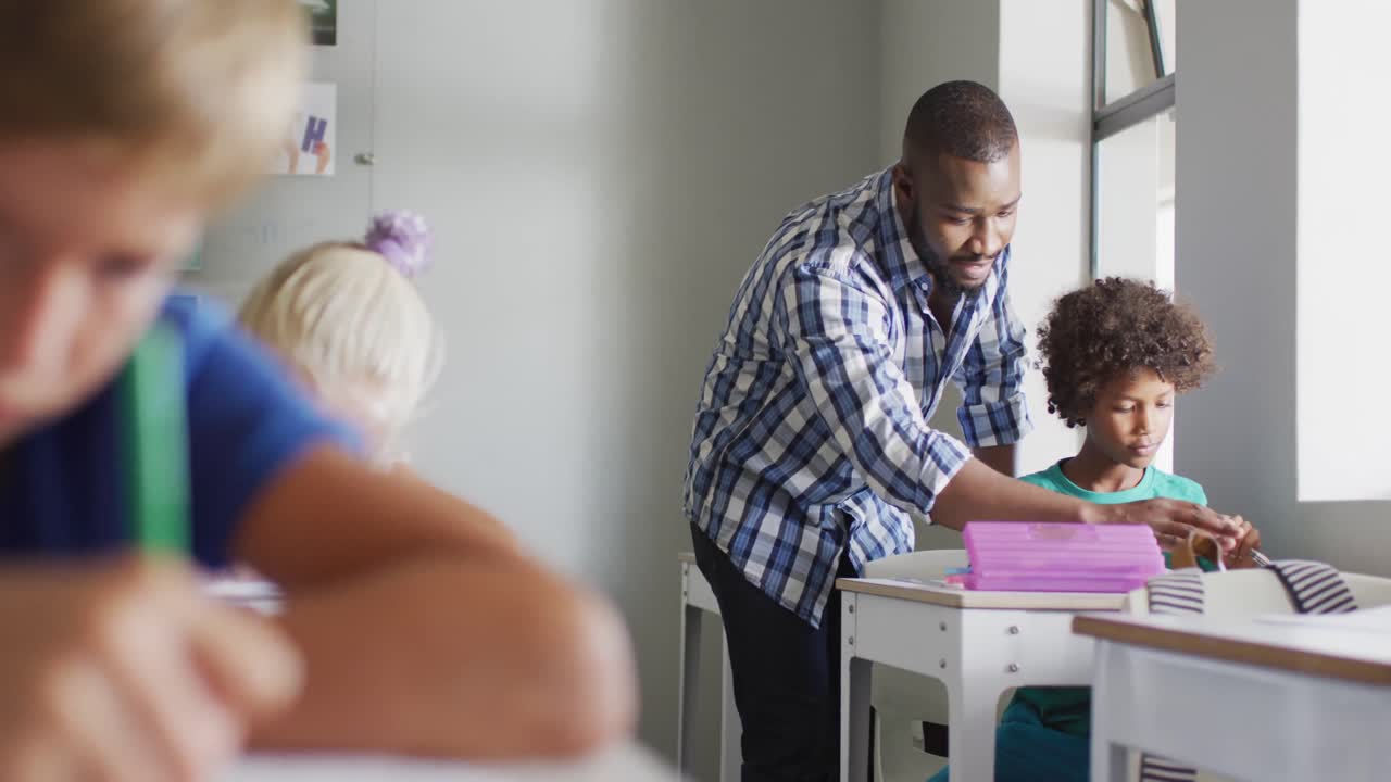 Video of happy african american male teacher helping biracial boy during lessons