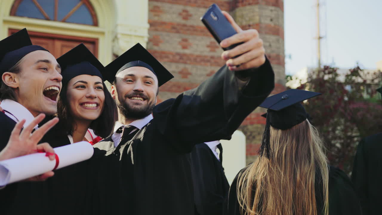 Portrait shot of the happy graduates making selfies with a smartphone near the University building