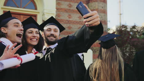 portrait shot of the happy graduates making selfies with a smartphone near the university building