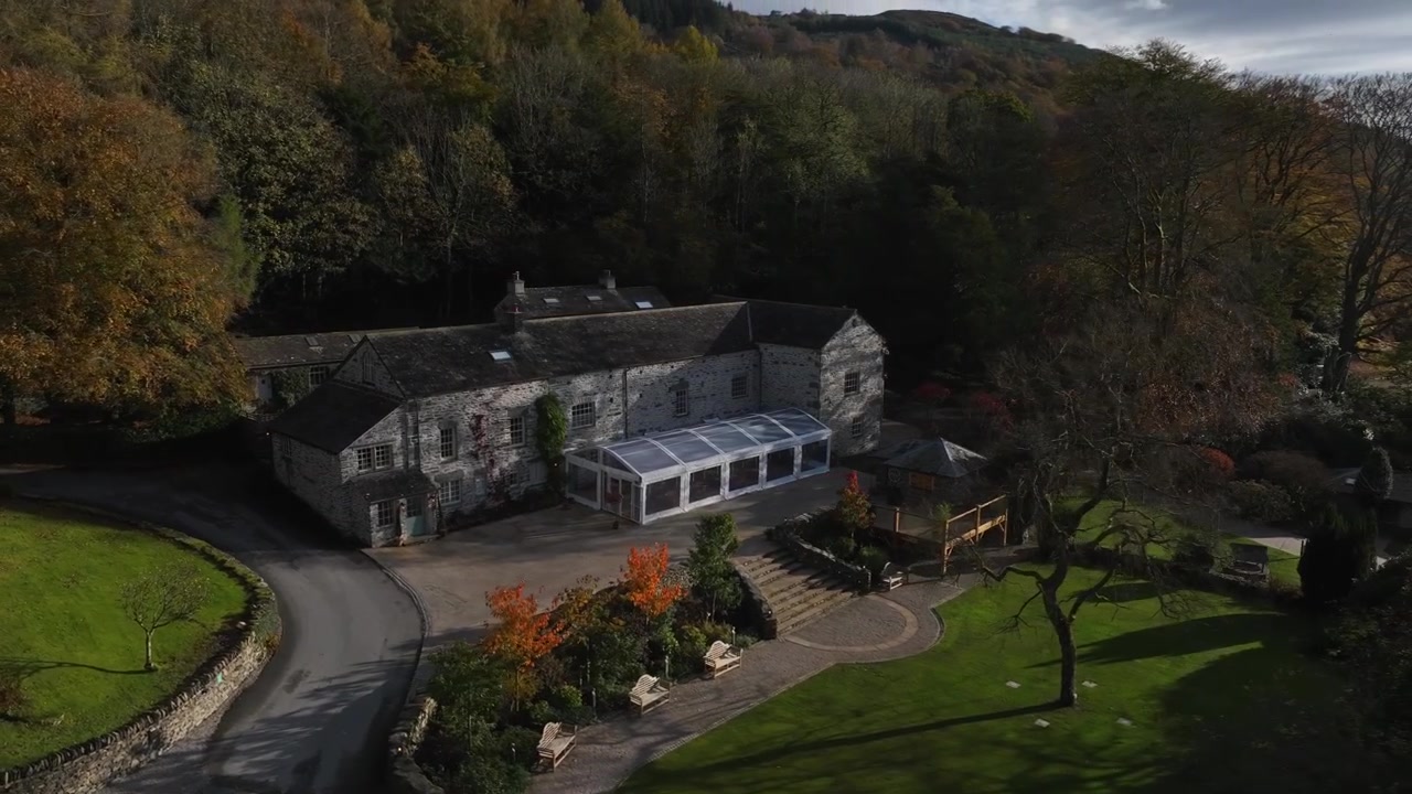 Domaine de Town Head, Windermere, Cumbria, Angleterre, novembre 2023. Un drone tourne dans le sens des aiguilles d'une montre au-dessus des arbres, révélant les bâtiments rustiques en pierre entourés d'une forêt dense avec des pelouses parfaites par une journée ensoleillée