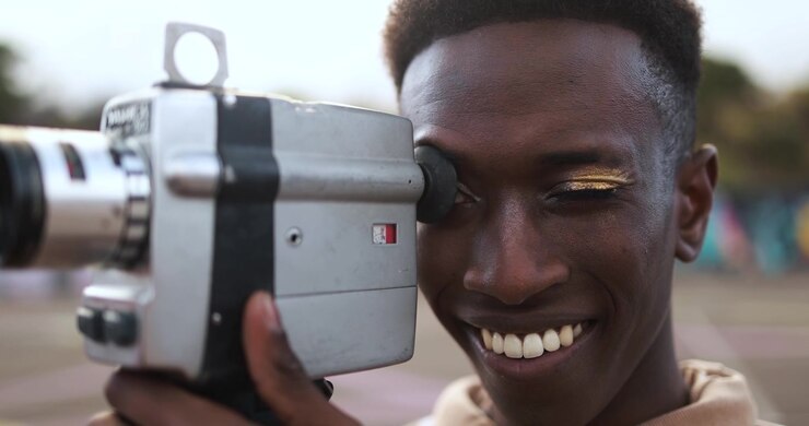 Smiling Young Black Man Filming with a Vintage Super 8 Camera