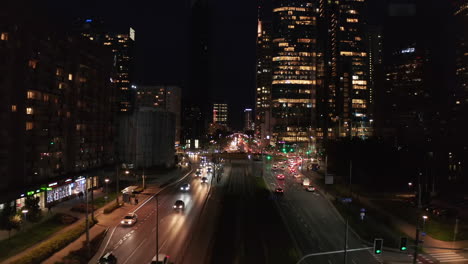 Fly-above-multilane-road-leading-through-large-town.-Cars-driving-in-street-and-intersection.-Night-city-scene.-Warsaw,-Poland