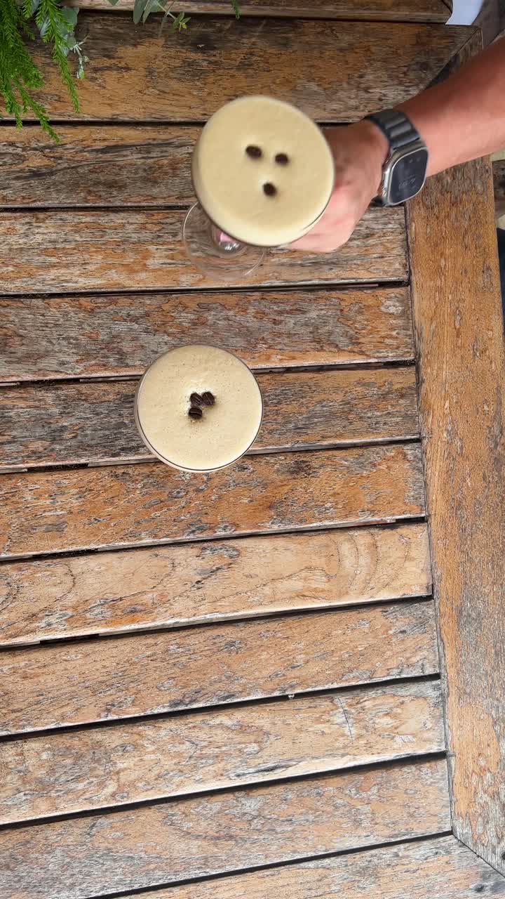Una mano si allunga verso un espresso martini su un tavolo di legno rustico, catturando un momento di attesa