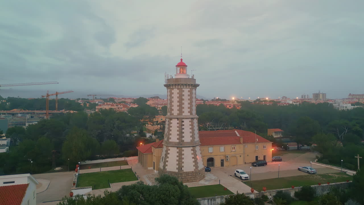 Pobřežní maják osvětlující pobřeží pod zataženou večerní oblohou, záběr dronem. Moderní maják.