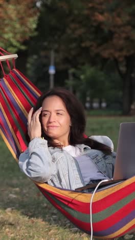 woman working on laptop in a hammock in a park