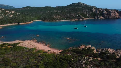 Holiday-sailing-ship-boats-in-a-beautiful-Mediterranean-sandy-beach-seaside-bay-with-crystal-clear-blue-turquoise-ocean-water-in-Sardinia,-Italy-and-little-waves