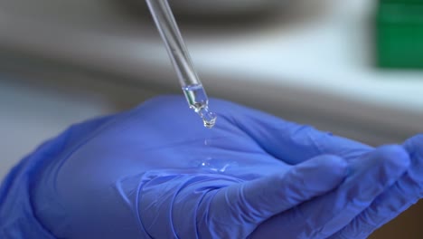 Close-up-dripping-a-liquid-into-a-gloved-hand-in-a-chemistry-science-lab