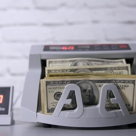 money counting equipment for paper money calculation. us dollar bills. woman putting money into counting machine at table indoors, close up