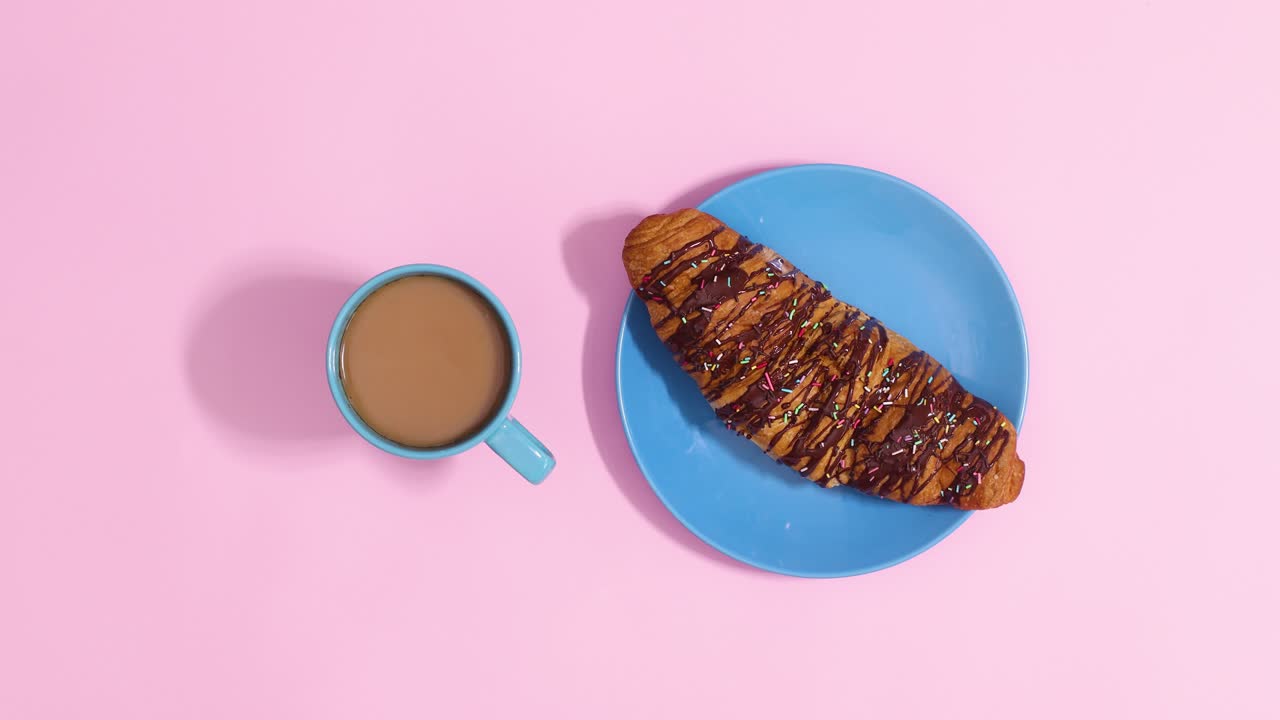 신선한 초콜릿 크로아산과 뜨거운 커피 컵이 파스텔 분홍색 배경에서 회전합니다.