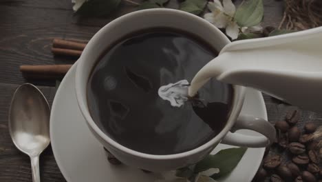 Pouring Cream into Black Coffee in Cup on Rustic Wooden Table