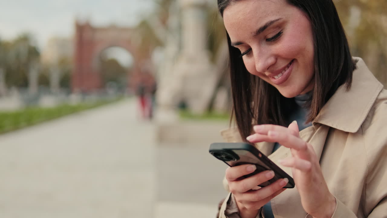 Giovane donna sorridente che scrive messaggi sullo smartphone all'aperto