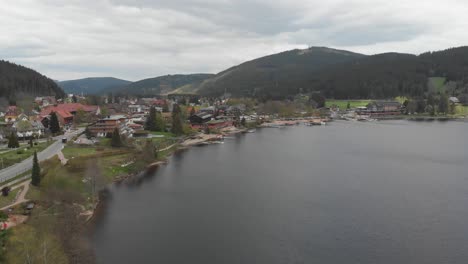 Luftschwenkansicht-Der-Straße-Und-Des-Sees-In-Dem-Kleinen-Dorf-Titisee,-Gelegen-In-Deutschland---Alte-Stadt,-Umgeben-Von-Wunderschönen-Bergen,-Die-Teil-Des-Schwarzwalds-Sind